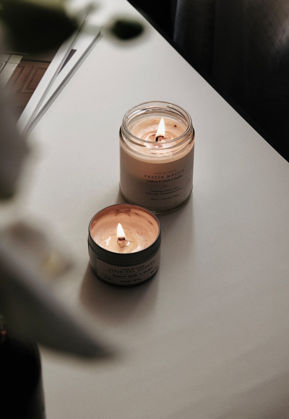 Two burning scented candles on a light-colored surface.